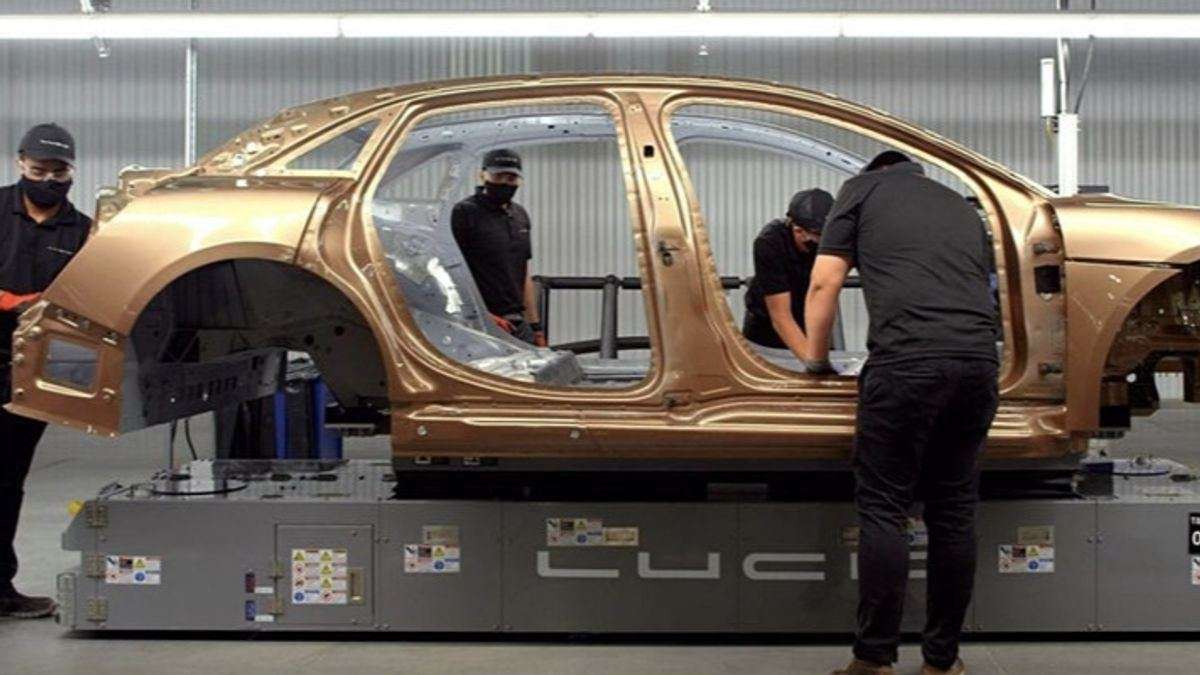 Image showing technicians in black Lucid uniforms assembling a gold Lucid Air Dream Edition. The car is a bare chassis at this point of its assembly.