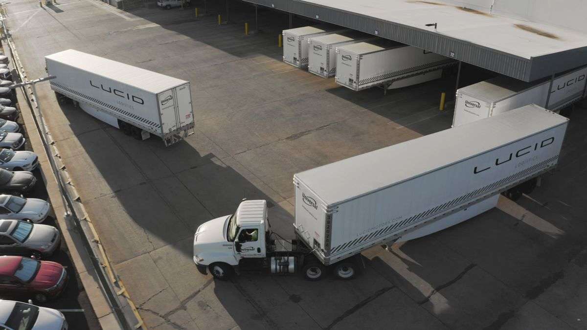 Image showing semi trucks with Lucid logos on their trailers pulling away from a loading depot.