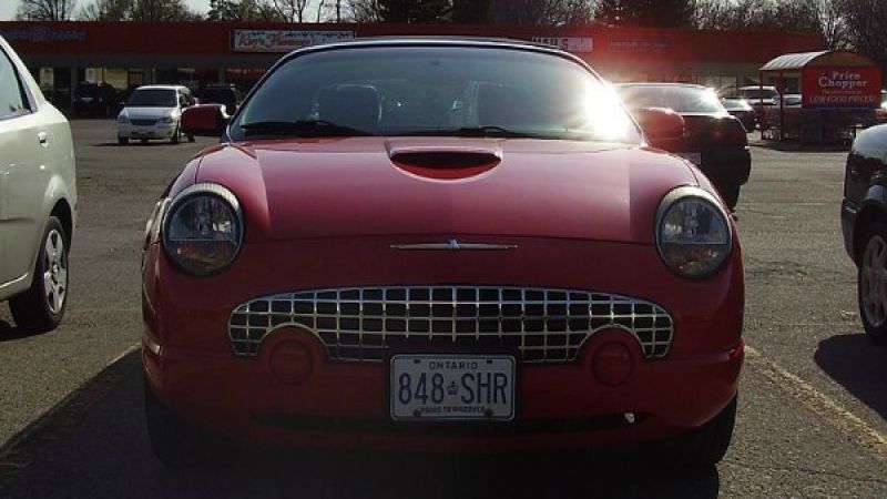 Red Ford Thunderbird (Canadian), model year 200x(?), front view taken at hood-level; sunlight from upper-left, glinting off the paint, chrome, & windshield.
