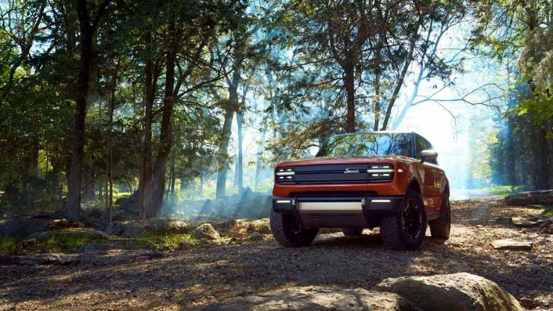 An orange Scout Traveler takes the path less traveled, a dirt road through the forest