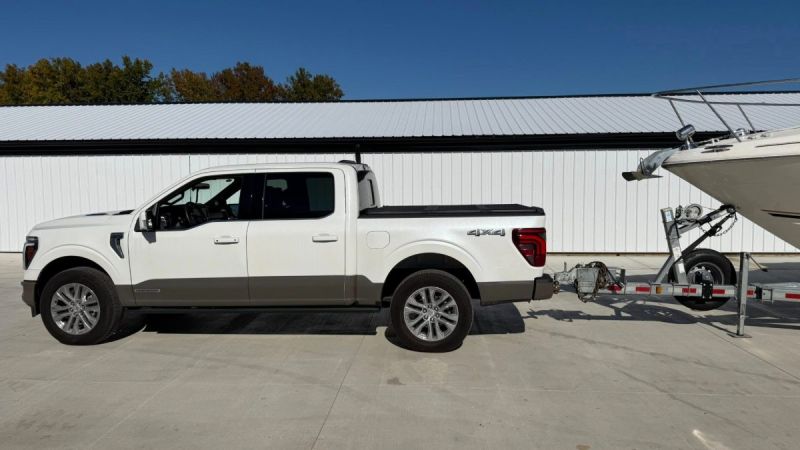 2021 Ford F-150 Platinum in Oxford White, side view, towing a trailer, parked outside white building with metal roof.