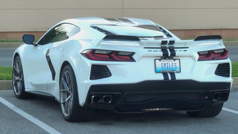 A white 2023 Chevrolet Corvette C8 with black racing stripes shown from the rear three-quarter view, featuring distinctive LED taillights and a Kentucky license plate.