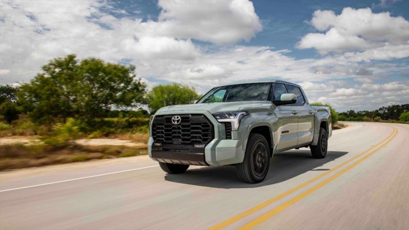 Sage green 2022 Toyota Tundra pickup truck driving on winding rural highway with cloudy blue sky and trees