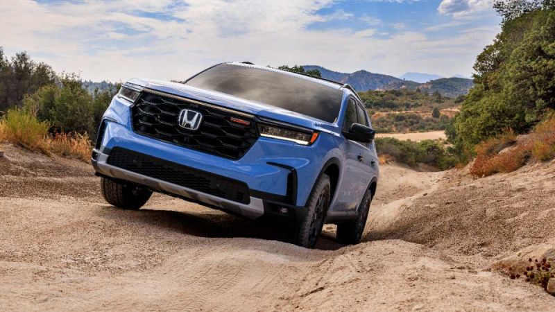 Blue Honda SUV navigating rugged dirt trail with mountain landscape and trees in background