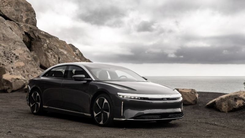 2023 Lucid Air luxury electric sedan in gray, front three-quarter view parked along a rocky coastal cliff with ocean backdrop.