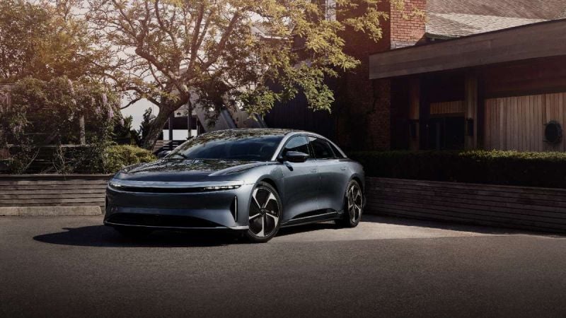 Silver 2023 Lucid Air Pure electric sedan parked near modern brick building with tree-lined background