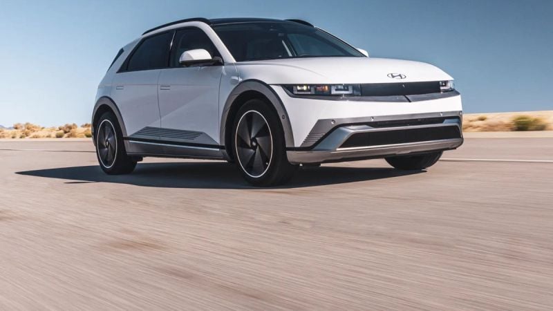 Front three-quarter view of a white Hyundai Ioniq 5 electric vehicle driving on an open desert road, highlighting its pixel LED headlights, clean front fascia, and crossover profile.