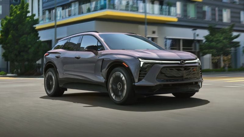2024 Chevrolet Blazer EV in metallic gray, angled front view, driving past modern urban buildings