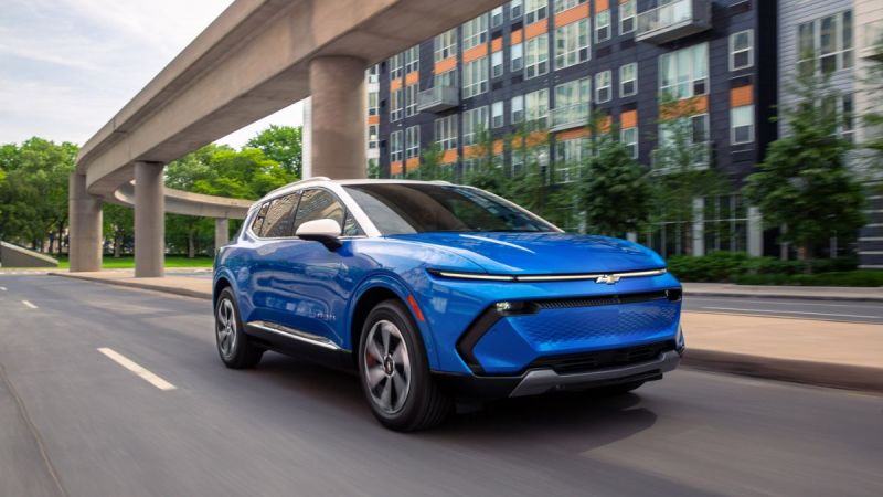 Blue Chevrolet electric SUV driving on urban street beneath elevated highway overpass