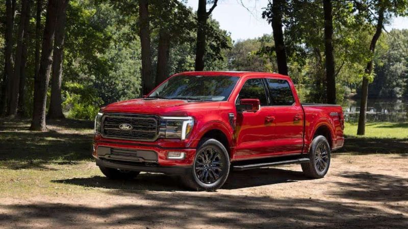 Red Ford F-150 parked in a shaded forest clearing near a lake, showcasing the truck’s front and side profile in natural outdoor lighting.