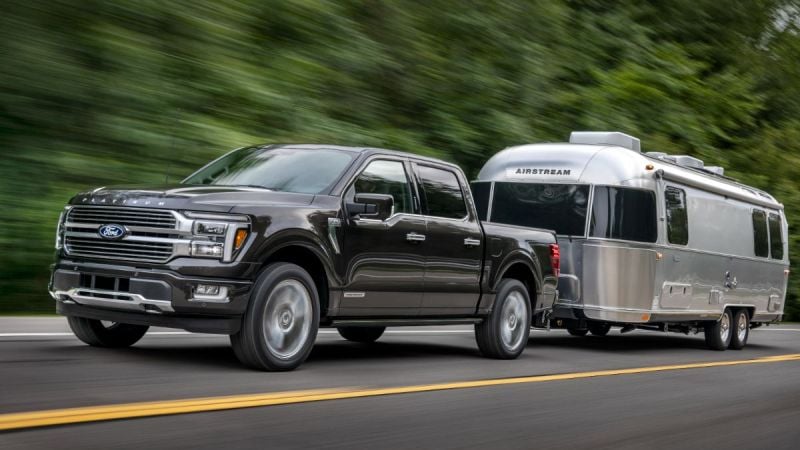 Black 2024 Ford F-150 Platinum towing an Airstream travel trailer, front three-quarter view demonstrating luxury and hauling capability.