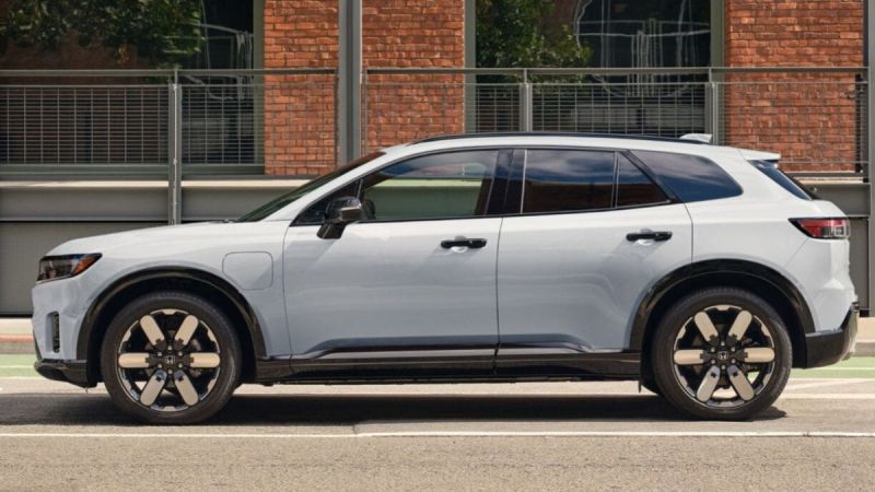 Side view of a Honda Prologue parked on a street with a white exterior and black accents. It stands in front of a brick building, conveying urban sophistication.