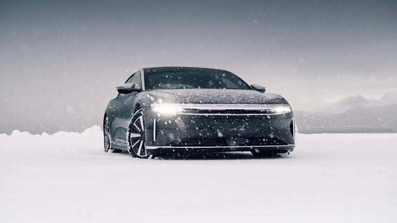 2024 Lucid Air electric sedan driving through snowy landscape in Norway, front view with illuminated LED light strip and winter performance setting.