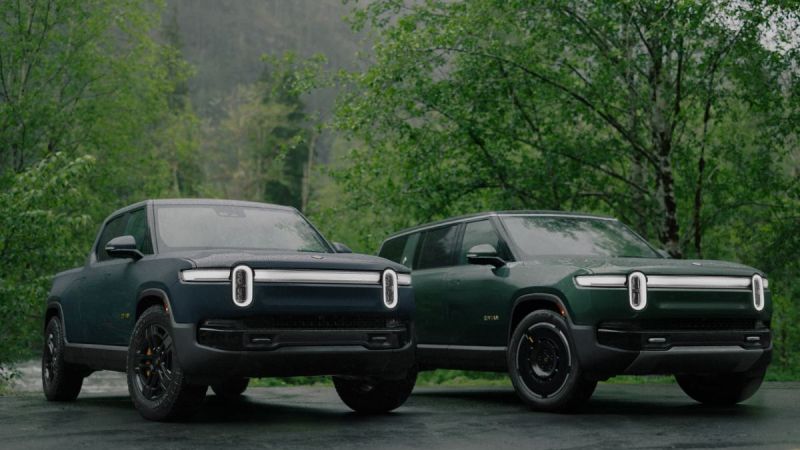 Two 2023 Rivian R1S And Rivian R1T electric pickup trucks in forest green, photographed from front 3/4 view, featuring distinctive LED light bars and black wheels, parked in wooded setting.