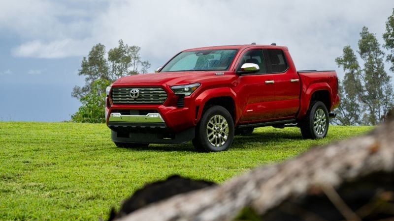 A red 2024 Toyota Tundra pickup truck is shown from a front three-quarter angle, positioned on a grassy hilltop against a cloudy sky backdrop.