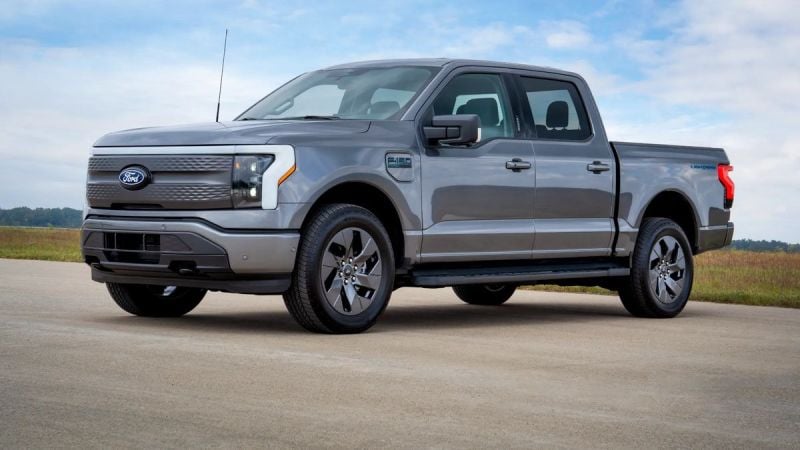 2024 Ford F-150 Lightning Flash trim in gray parked on a paved road with a grassy field and blue sky in the background.
