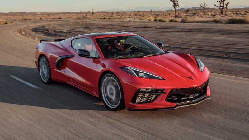 Red Chevrolet Corvette C8 driving at speed on an open desert highway, highlighting aerodynamic styling, low stance, and performance-focused front fascia.
