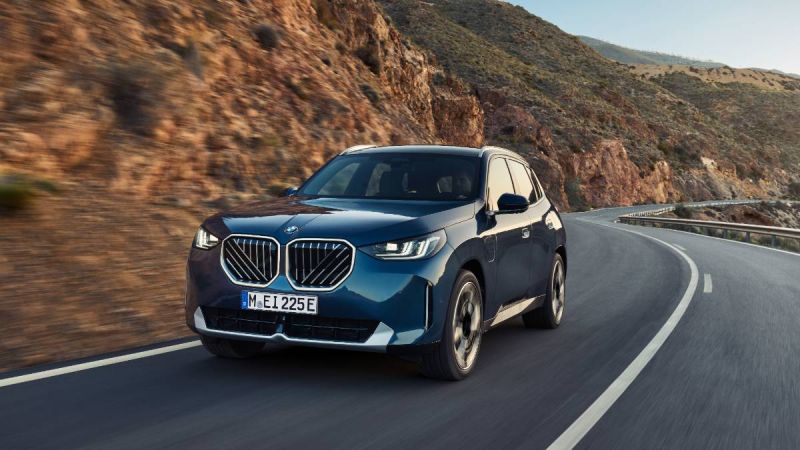 Dark blue BMW x3 SUV curving along mountain road with rocky terrain and guardrail
