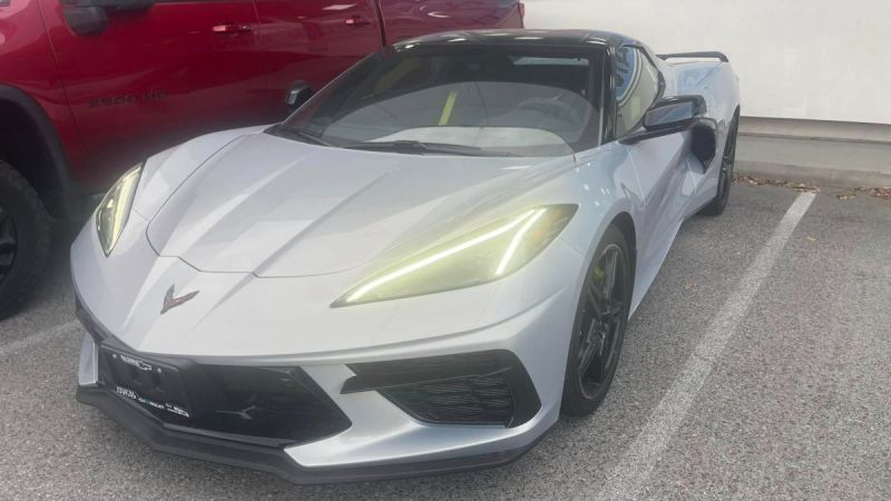 2023 Chevrolet Corvette C8 in Arctic White, front three-quarter view, featuring angular LED headlights and aggressive black front splitter, parked in covered lot.