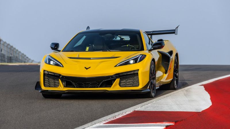 2025 Chevrolet Corvette Z06 in yellow driving aggressively on a race track, shown from a dynamic front angle with a large rear wing.