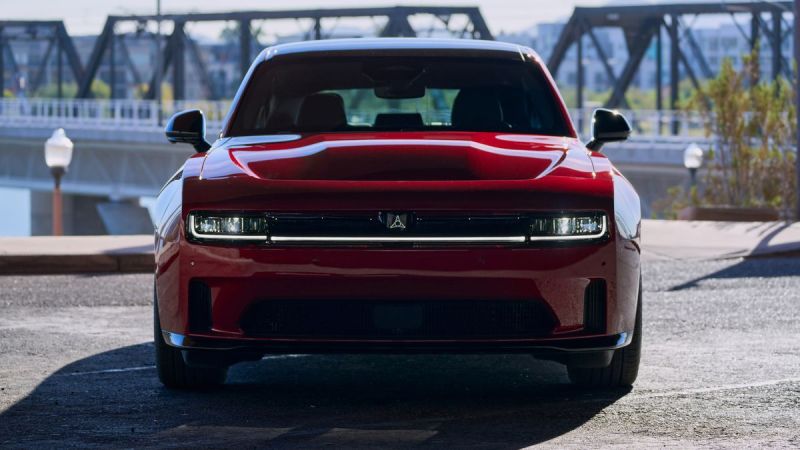 A red car with a sleek design and prominent grille, parked near a bridge in bright daylight, showcasing its modern features.