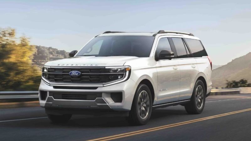 A white Ford Expedition drives on a scenic road with mountains and trees in the background, under a clear sky, conveying a sense of adventure and freedom.