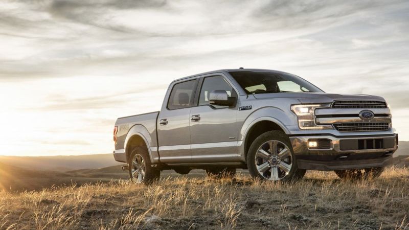 Silver 2025 Ford F-150 pickup truck photographed at three-quarter front angle on hilltop during sunset, featuring chrome grille, LED headlights, and premium wheels.