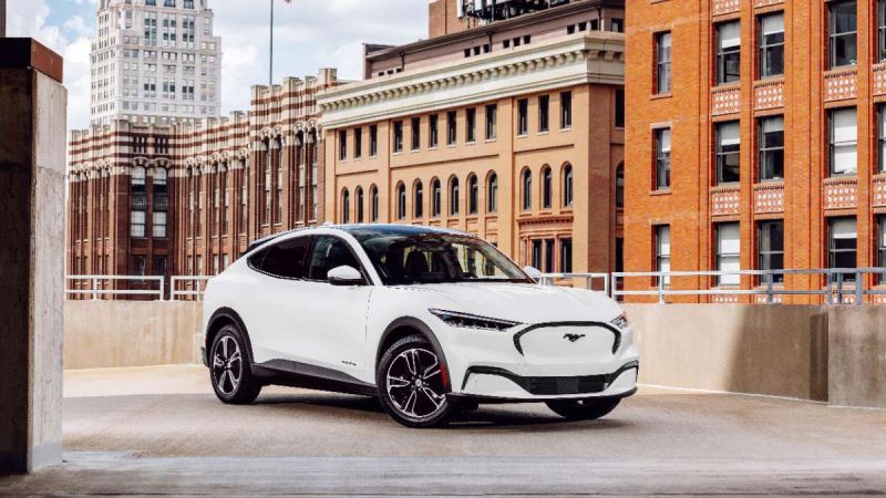 White Ford Mustang Mach-E electric SUV parked on urban rooftop with historic brick buildings in background