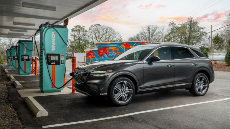 Dark gray Genesis GV70 SUV parked at Ionna charging station during sunset with vibrant pink and orange sky