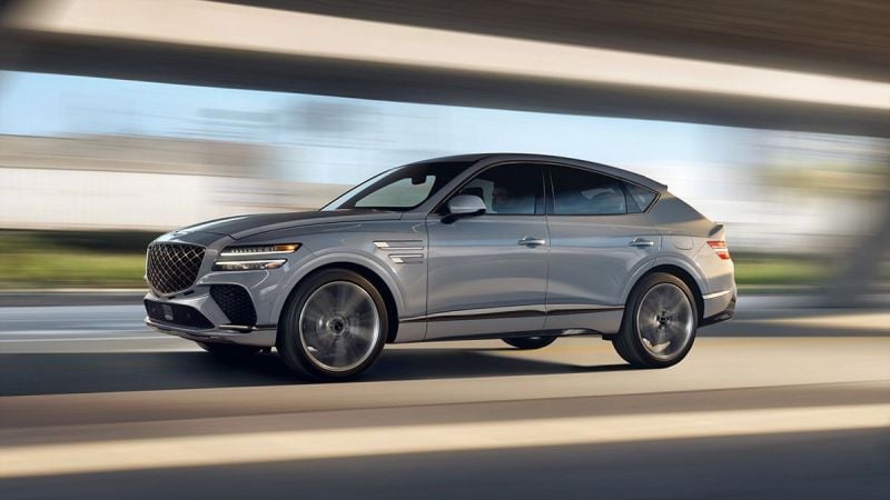 Silver Genesis GV80 SUV in motion, showcasing dynamic side profile with blurred urban background
