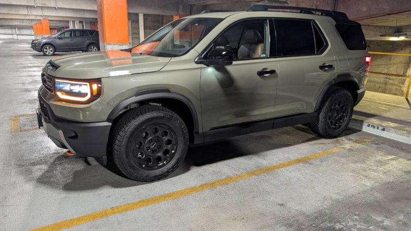 2025 Honda Passport TrailSport in olive green, side view in parking garage, featuring black off-road wheels, LED headlights, and rugged all-terrain tires.