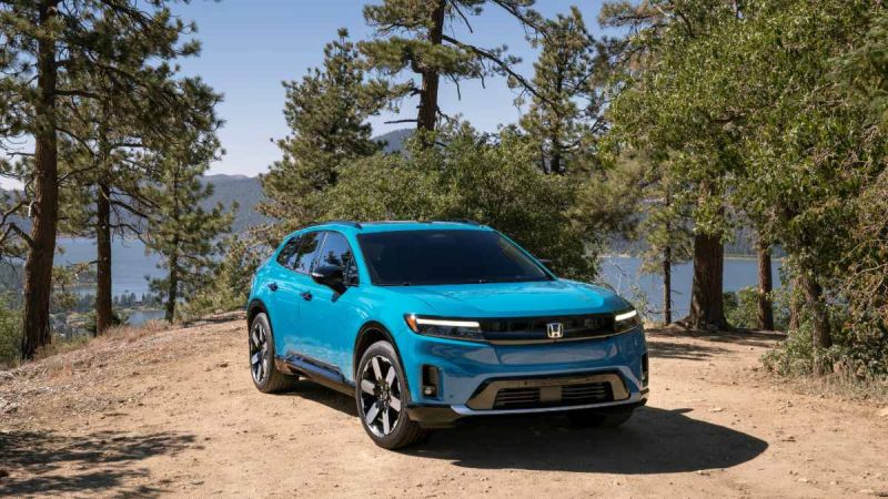 2024 Honda Prologue in bright turquoise blue, front three-quarter view, showcasing sleek LED headlights and modern crossover design, photographed on mountain overlook with pine trees and lake backdrop.