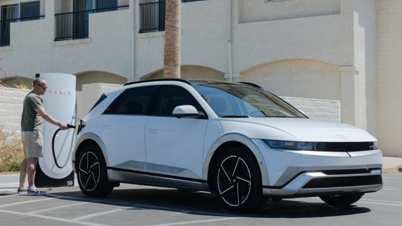 White 2025 Hyundai Ioniq 5 charging at a Tesla Supercharger station in a parking lot.