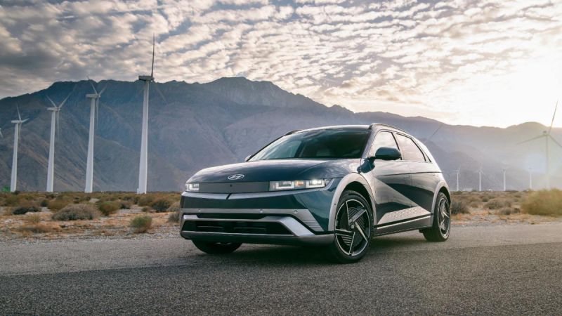 Electric car parked on a road with wind turbines and mountains in the background.