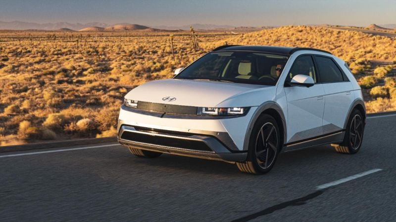 White Hyundai IONIQ 5 electric SUV driving on desert highway at golden sunset with mountains