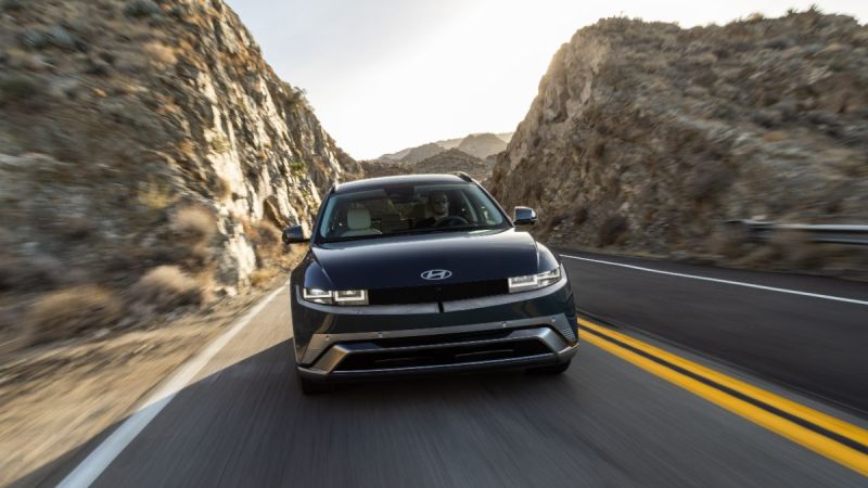 Blue Hyundai SUV driving on mountain road between tall rocky cliffs at sunset
