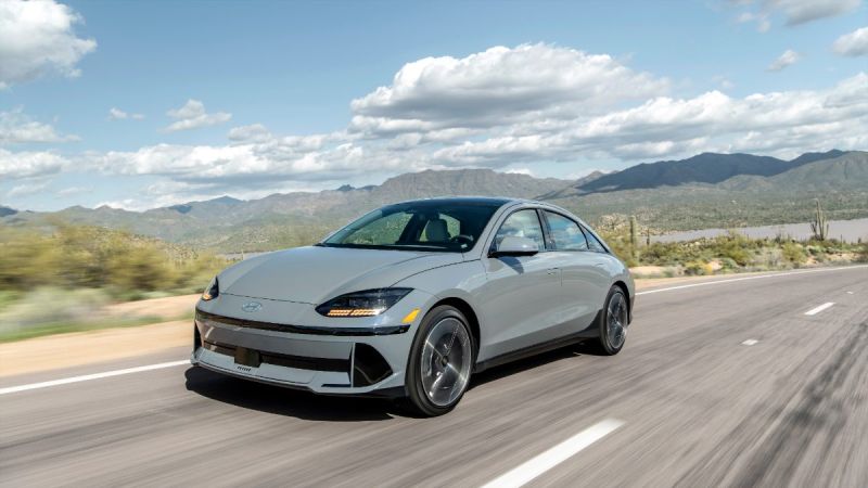 Silver 2025 Hyundai Ioniq 6 driving on desert highway with mountain backdrop, aerodynamic profile and modern design