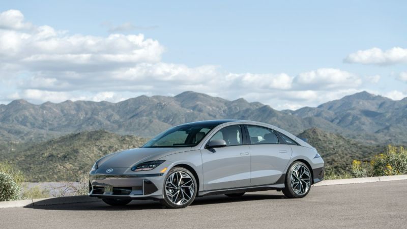 Silver sedan parked on a road with mountains and cloudy sky in the background.