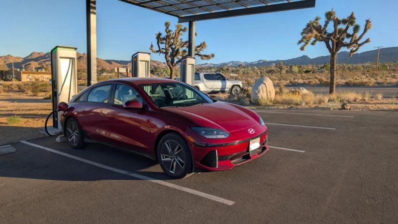 Red 2025 Hyundai Ioniq 6 electric sedan parked at charging station in Joshua Tree desert, mountains visible, three-quarter front view.
