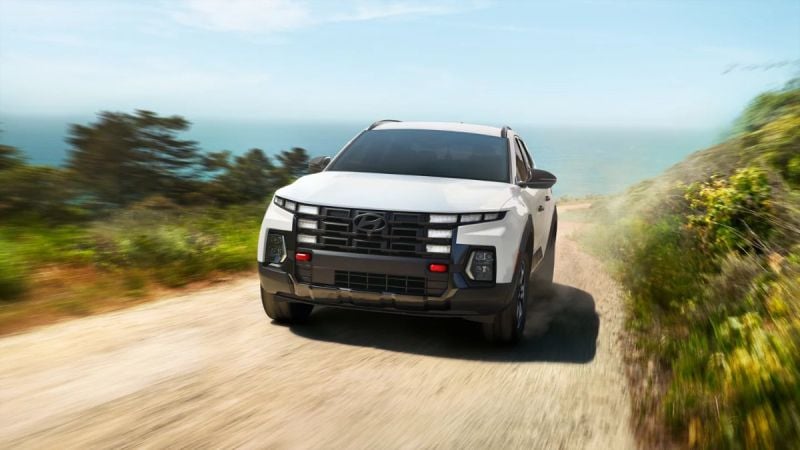 White Hyundai Tucson driving on dusty coastal road with blurred greenery and ocean horizon