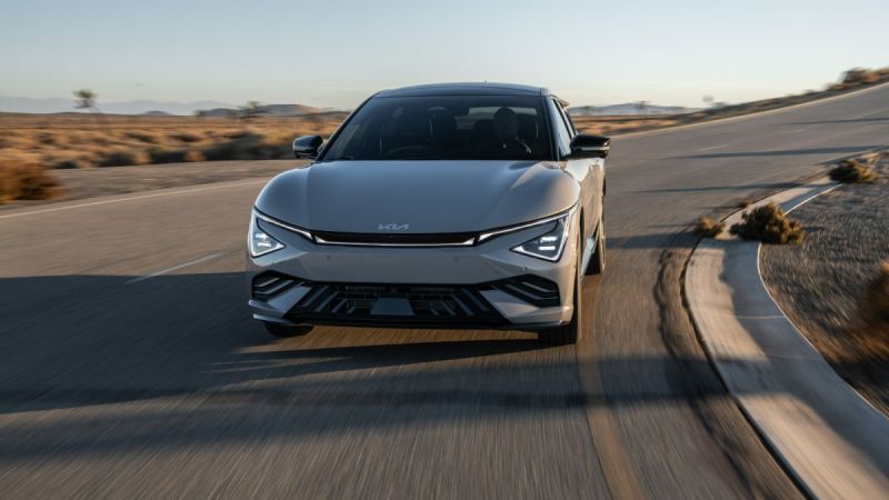 Silver Kia EV6 driving on winding desert road at sunset, front view