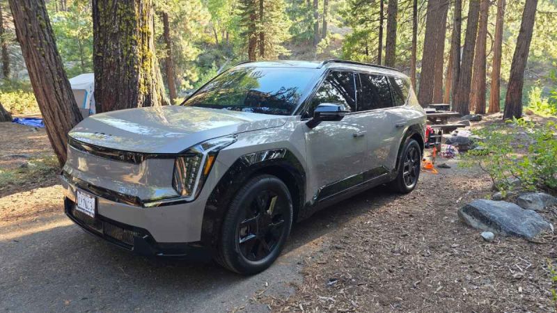 A silver SUV parked at a forest campsite with trees and a picnic table nearby.