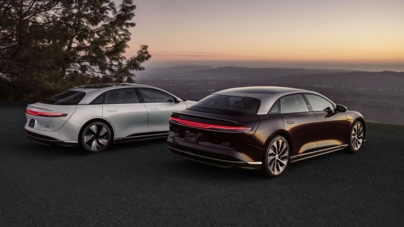 Two sleek, modern electric cars in white and dark tones parked against a scenic sunset backdrop, showcasing elegant design features.