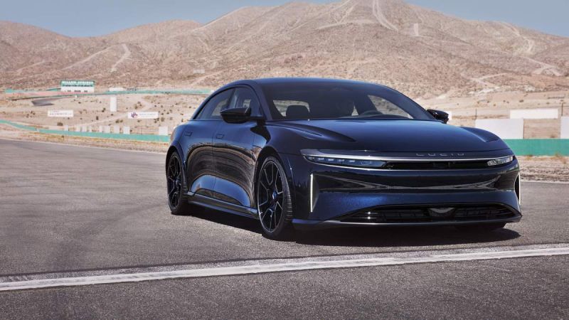 A sleek black Lucid Air luxury electric vehicle parked on a racetrack, with desert mountains in the background under a clear blue sky.