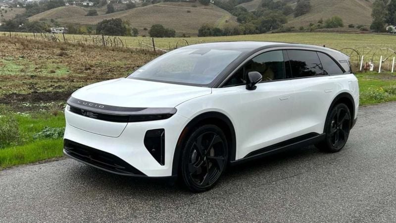 2025 Lucid Gravity electric SUV in pearl white, shown at three-quarter front angle on rural mountain road, featuring sleek aerodynamic design and black contrast elements.