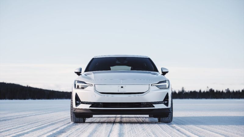 2025 Polestar 2, front view in snow, featuring a white exterior, distinctive headlights, and a minimalist grille.