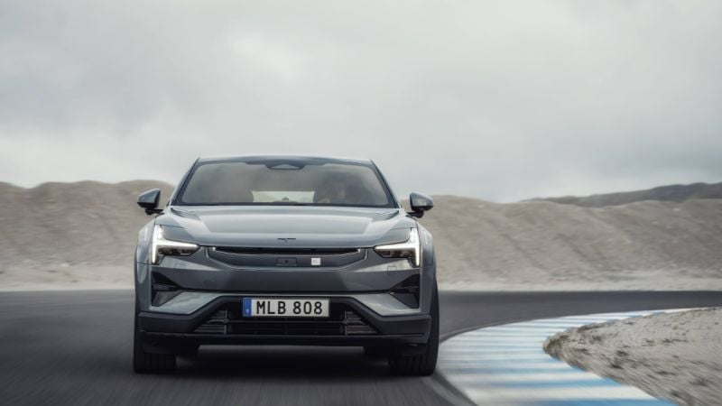 Silver car driving on a curved road with a mountainous background under cloudy skies.