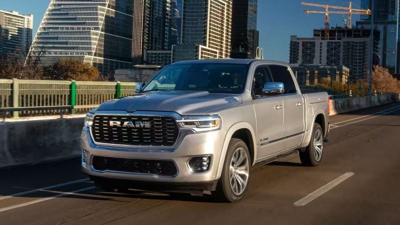 Silver 2025 RAM 1500 pickup truck driving on a city bridge with modern skyscrapers in the background. The scene conveys a sense of urban adventure.