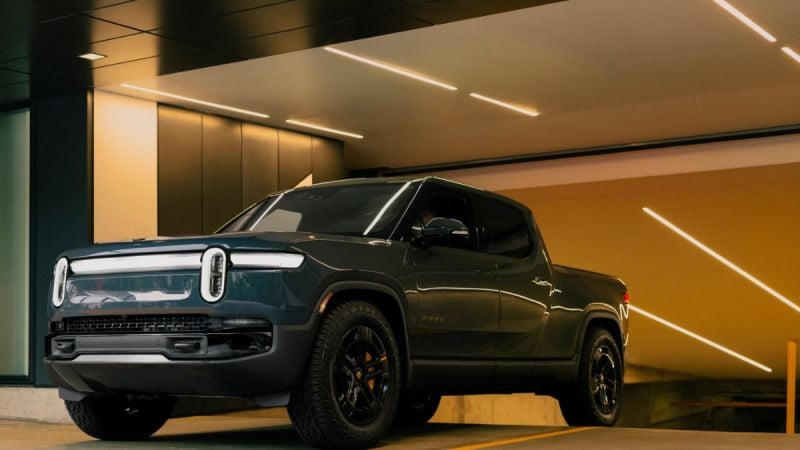 Dark blue Rivian R1T electric pickup truck parked in modern architectural space with diagonal lighting and yellow walls