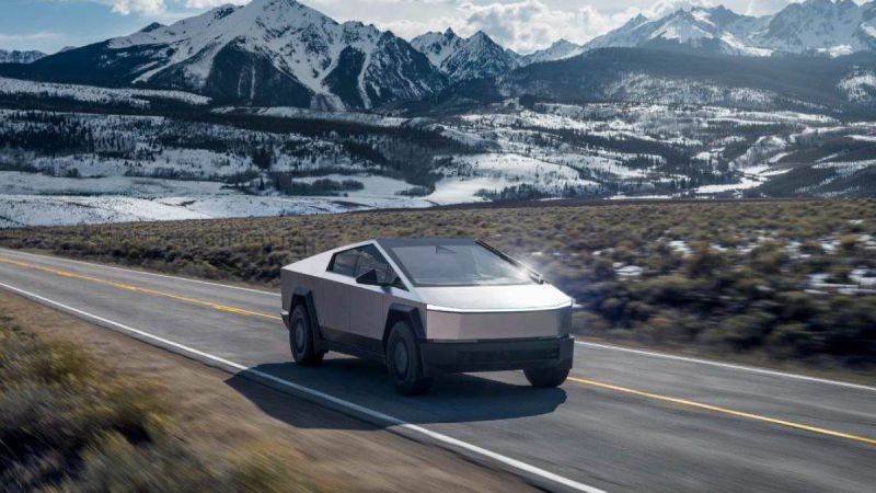 Tesla Cybertruck driving on mountain highway with snow-capped peaks and winter landscape backdrop